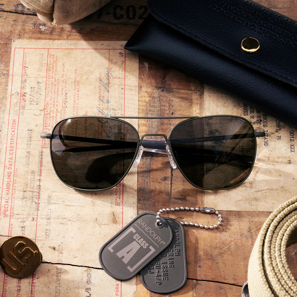 แว่นตา Randolph รุ่น Aviator Military Olive & American Gray วางอยู่บนโต๊ะ พร้อมกล่องแว่น